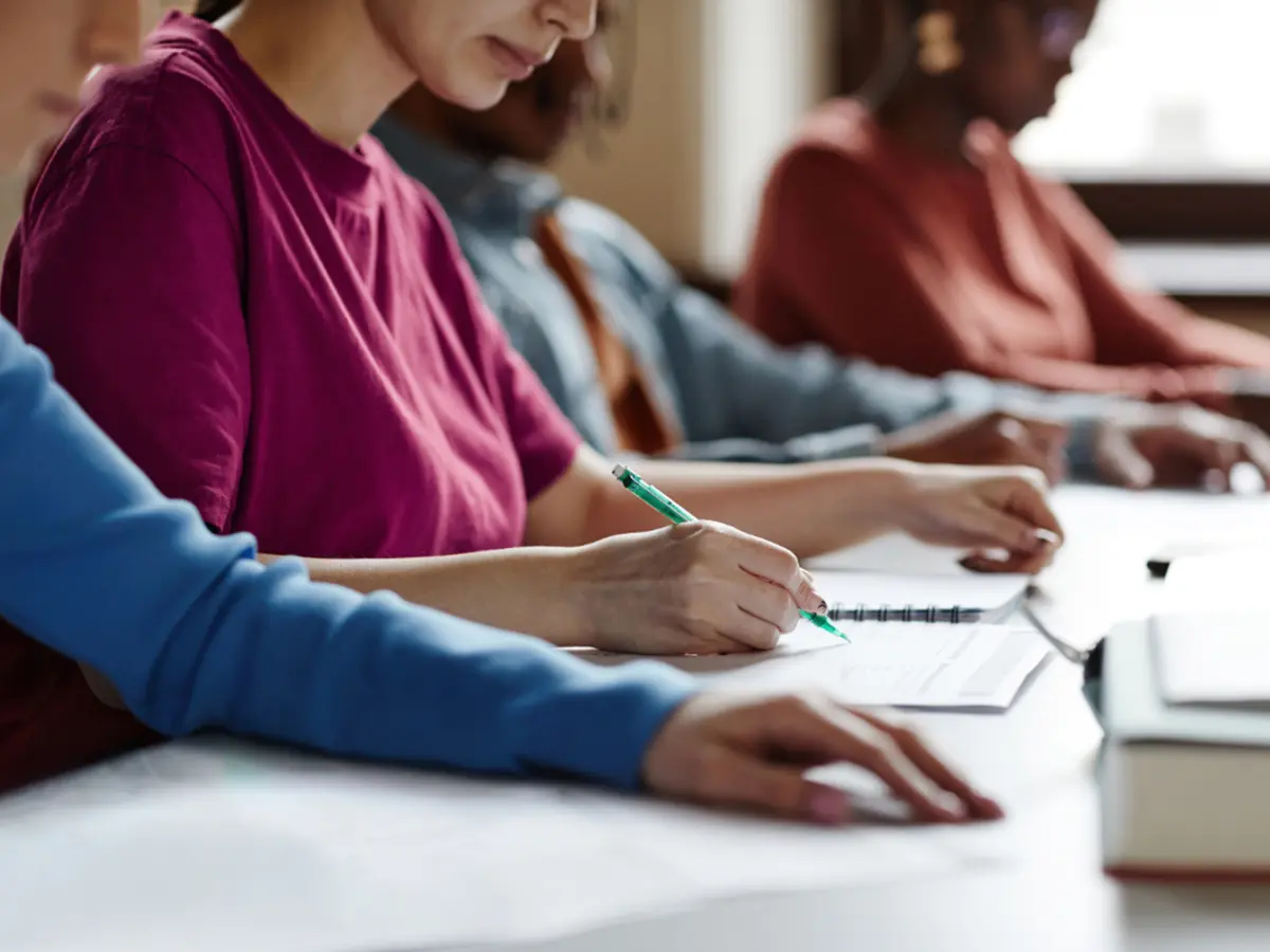 Four individuals are engaged in a study session, focused on writing notes in notebooks and textbooks on a table.