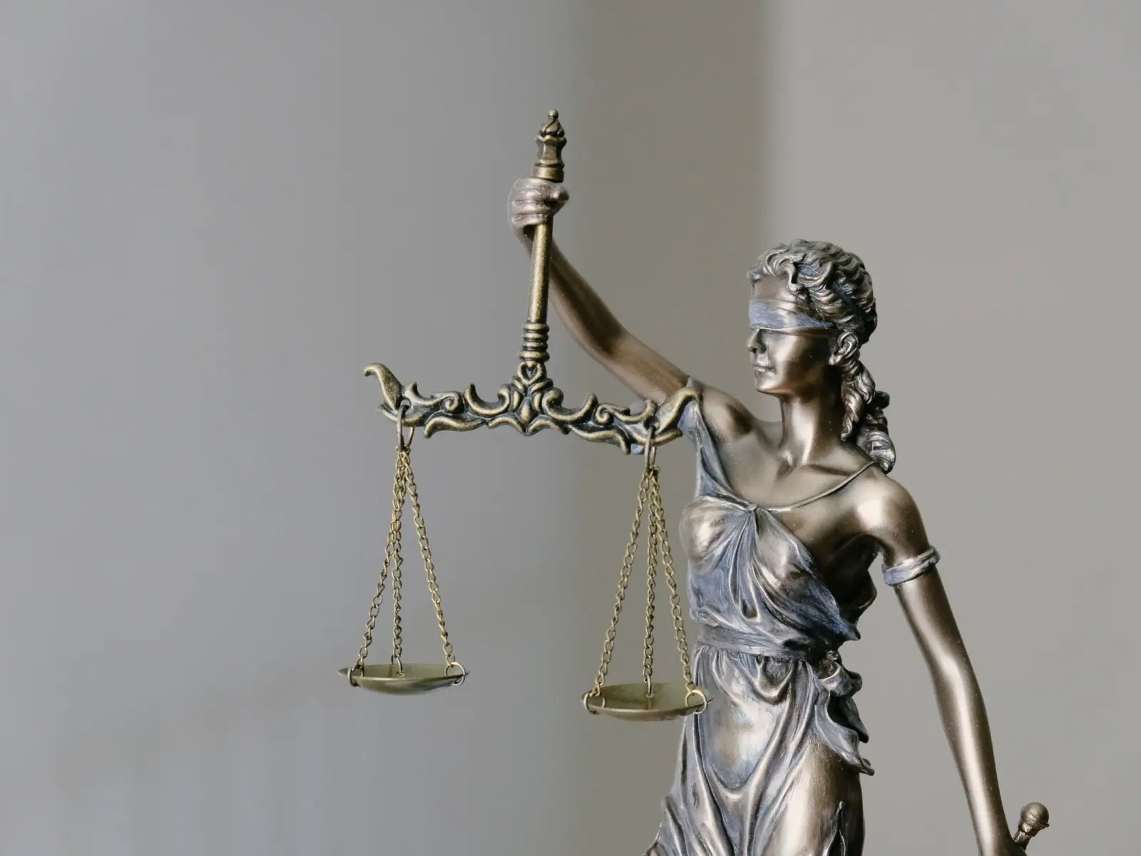 A bronze statue of Lady Justice holding balanced scales, blindfolded and draped in flowing robes, symbolizing fairness and integrity.