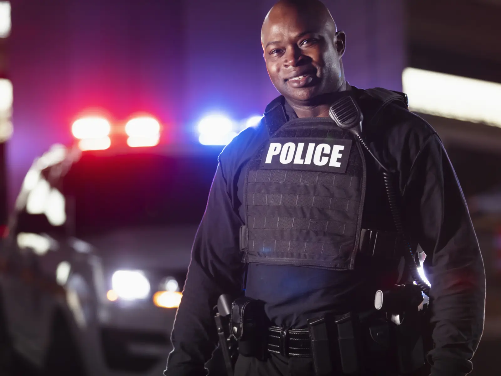 Image of male police officer standing in front of police car.