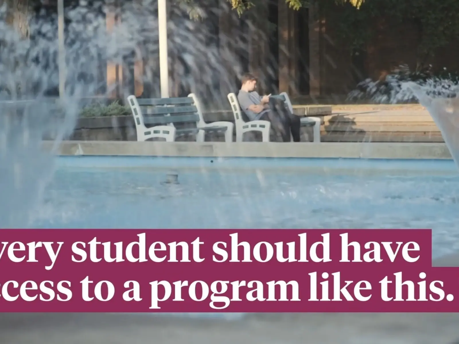 Fountain jets in a plaza with a person on a bench in the background and an overlaid caption about every student having access to a program.