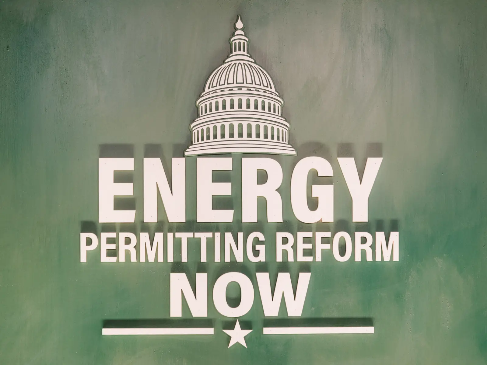 White Energy Permitting Reform Now text under a U.S. Capitol dome icon on a textured green background, like a political campaign sign