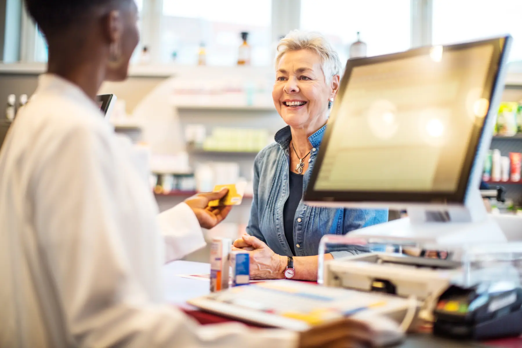 A female pharmacist returning credit card to elderly woman.
