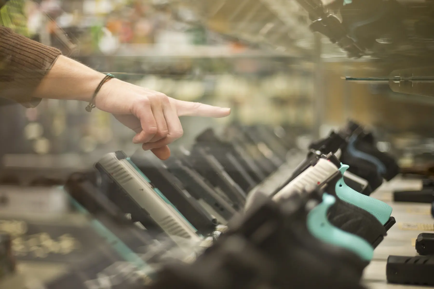 Customer pointing at hand gun through glass case.