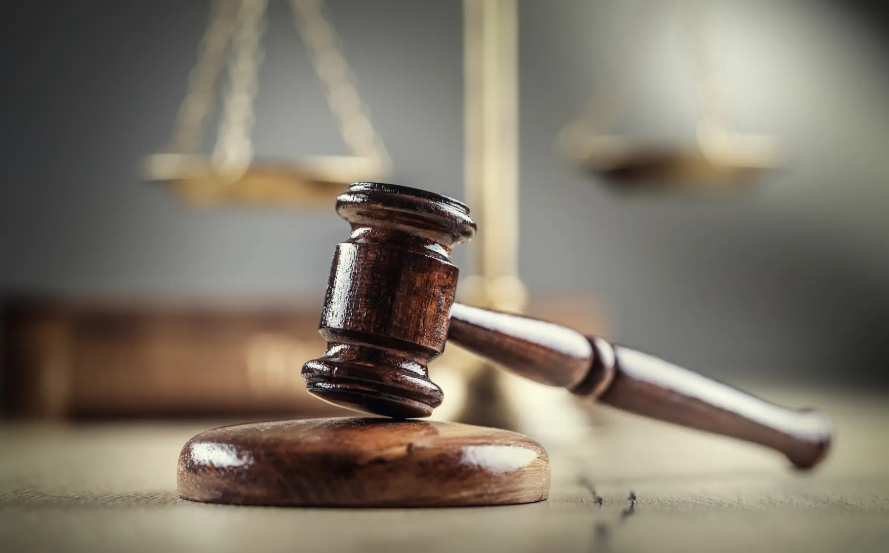 A wooden gavel rests on a circular block, with blurred scales of justice in the background, symbolizing law and order.