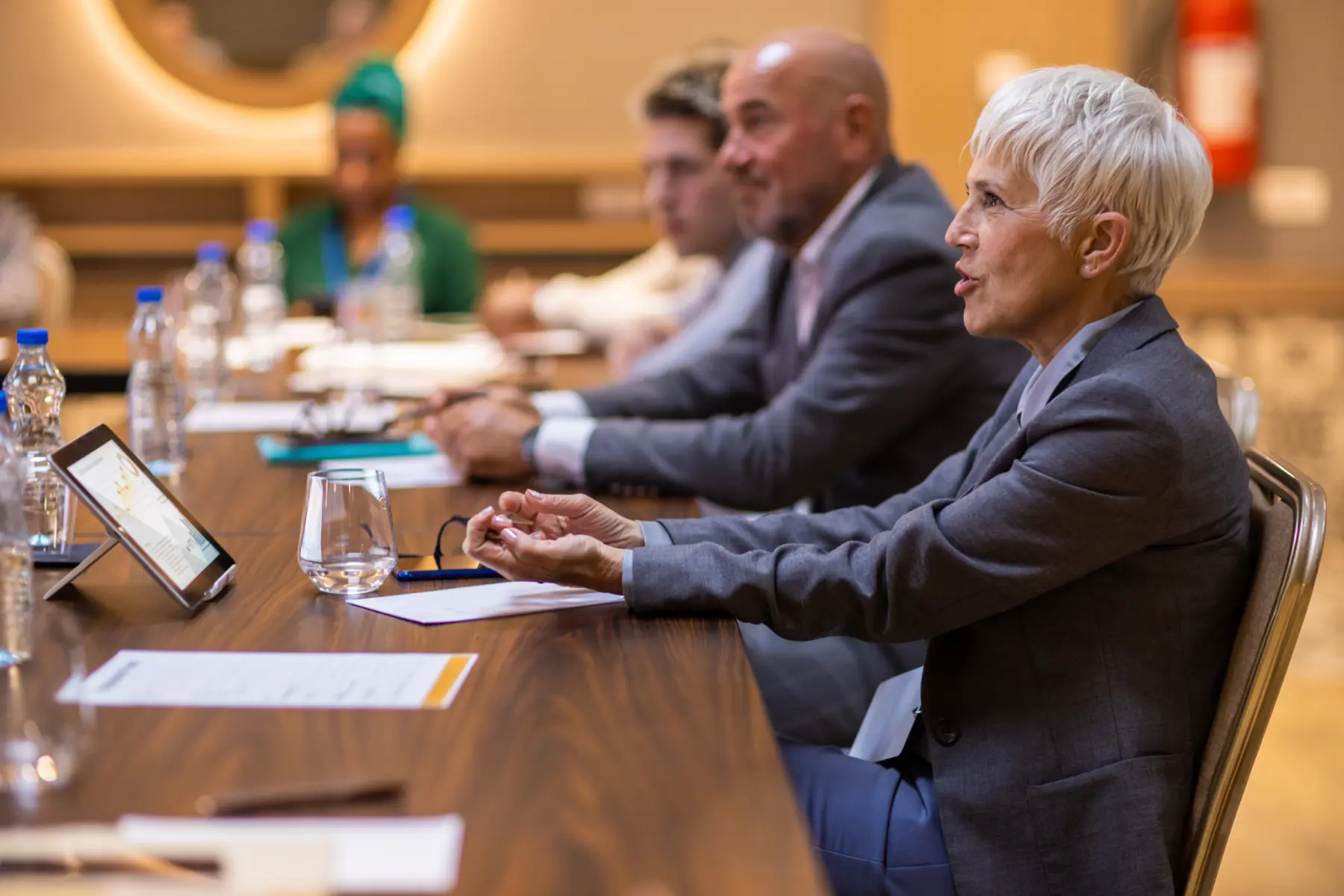 A professional meeting scene with a diverse group of people seated at a long table, actively engaging and sharing ideas.