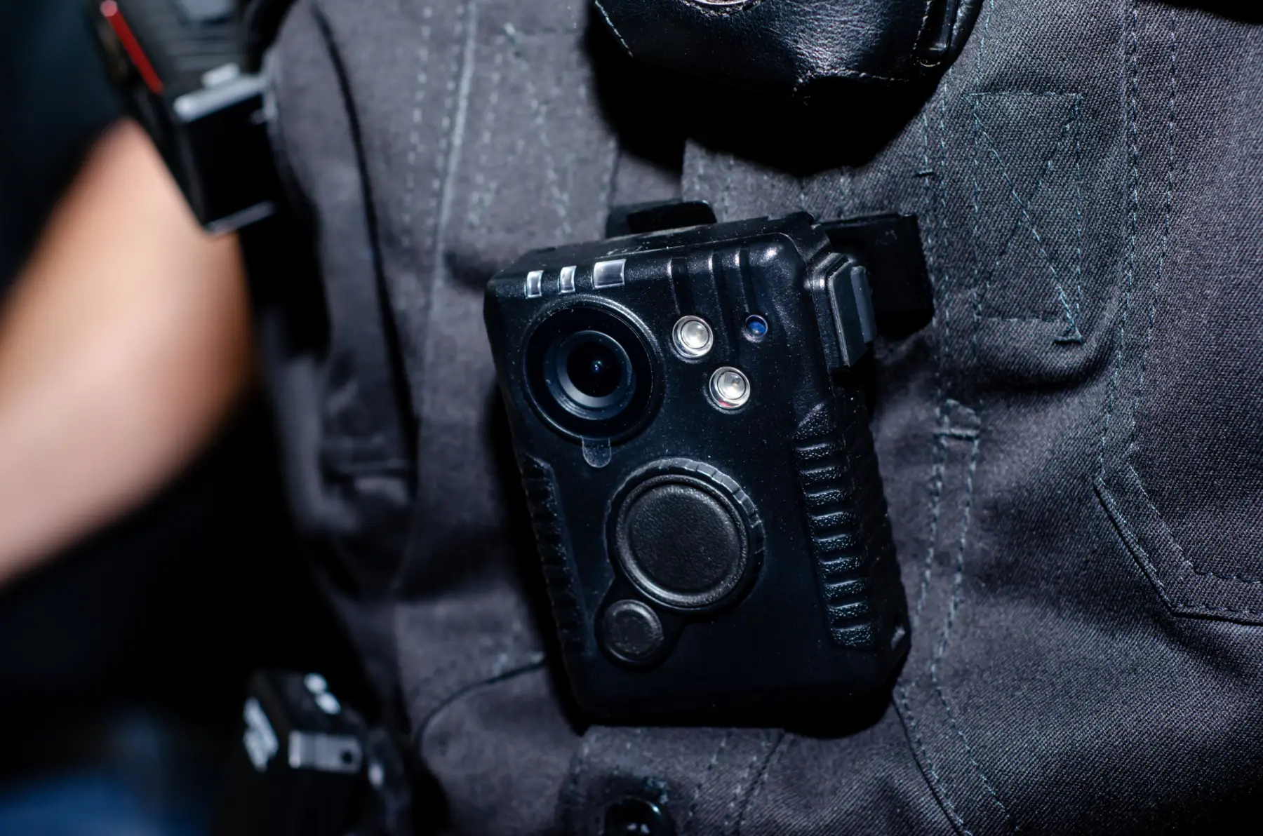 A black body camera is securely attached to a dark uniform, featuring a lens and buttons for operational controls.
