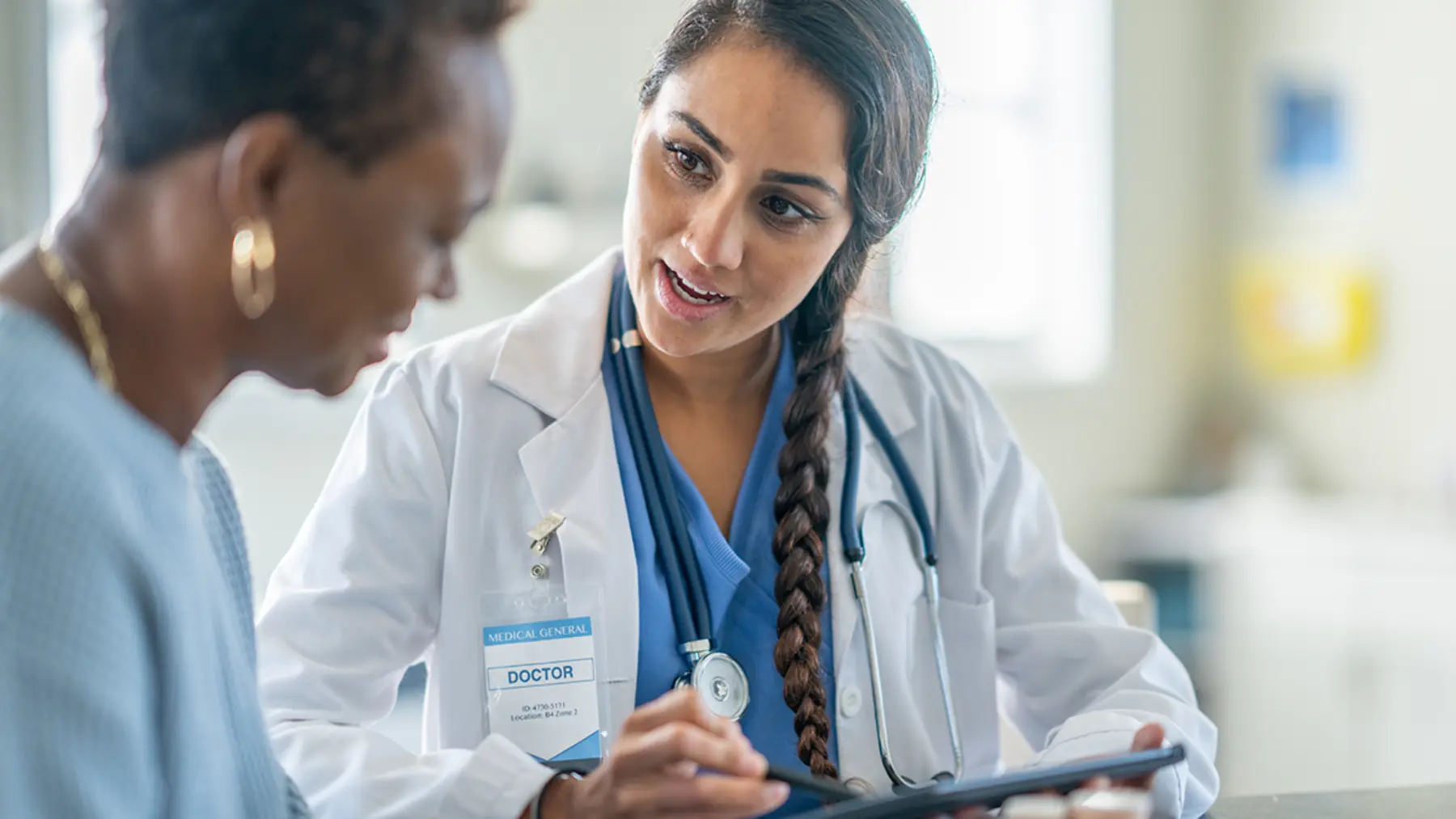 A doctor in a white coat explains information on a tablet to a patient, fostering a focused and empathetic conversation.