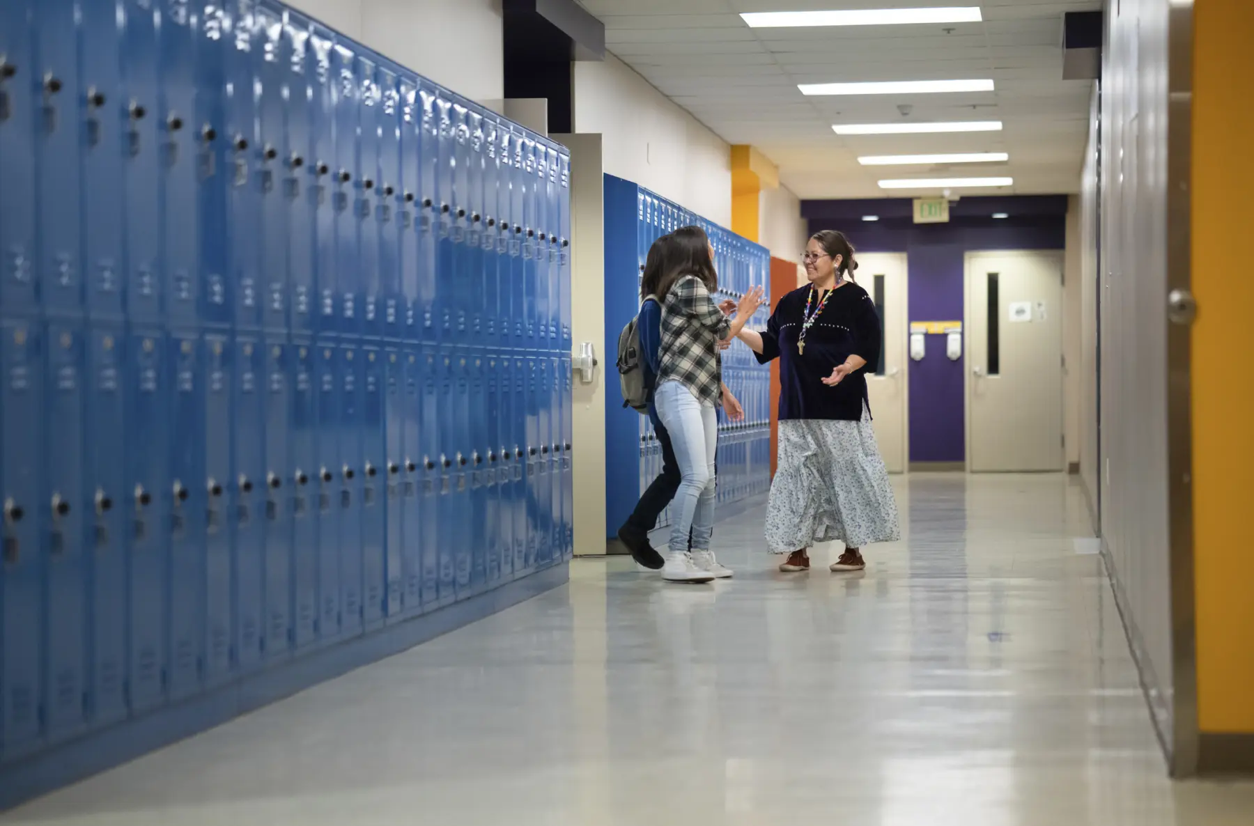 Image of teacher talking with students in hall of school.