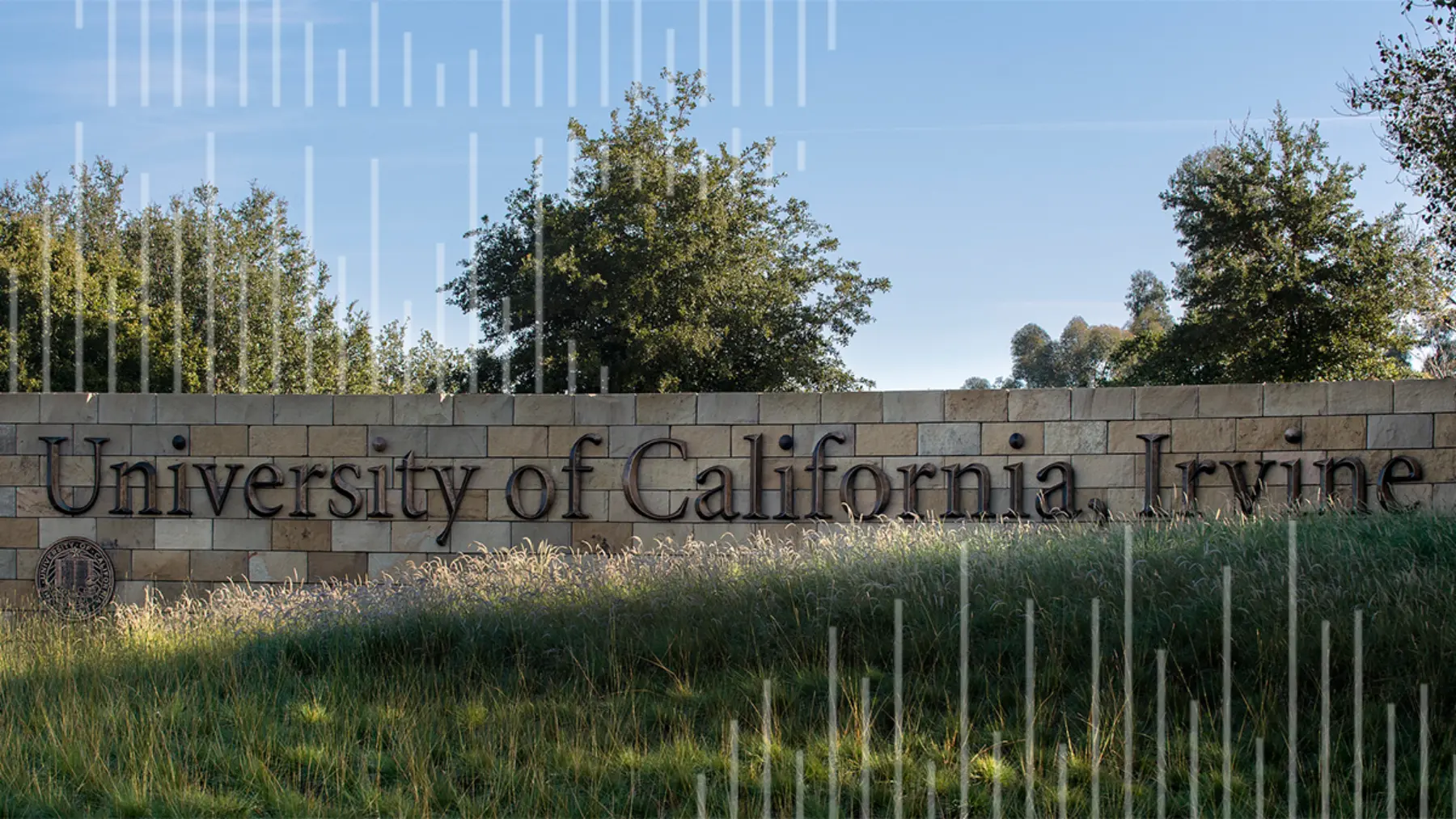 A stone wall features the engraved text "University of California, Irvine," surrounded by greenery and a clear blue sky above.