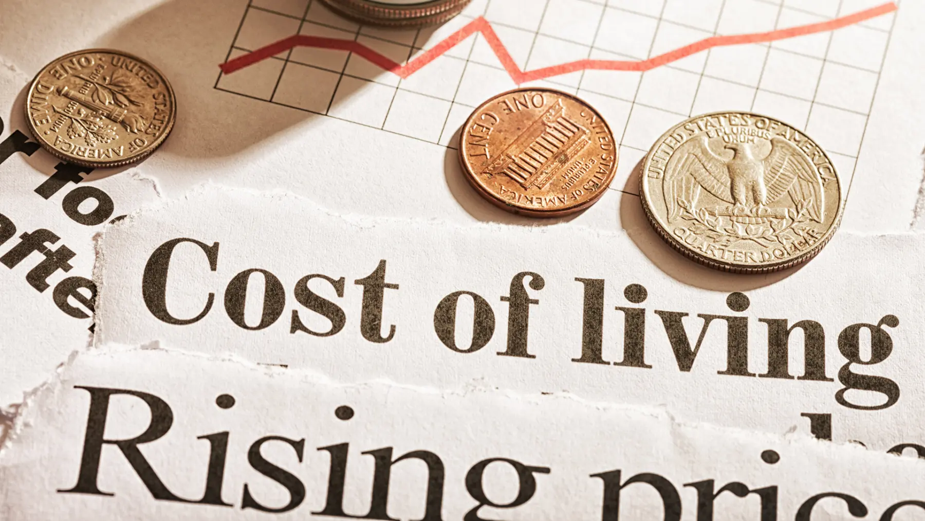 Coins are placed on torn newspaper headlines discussing the rising cost of living and prices, alongside a red line graph.