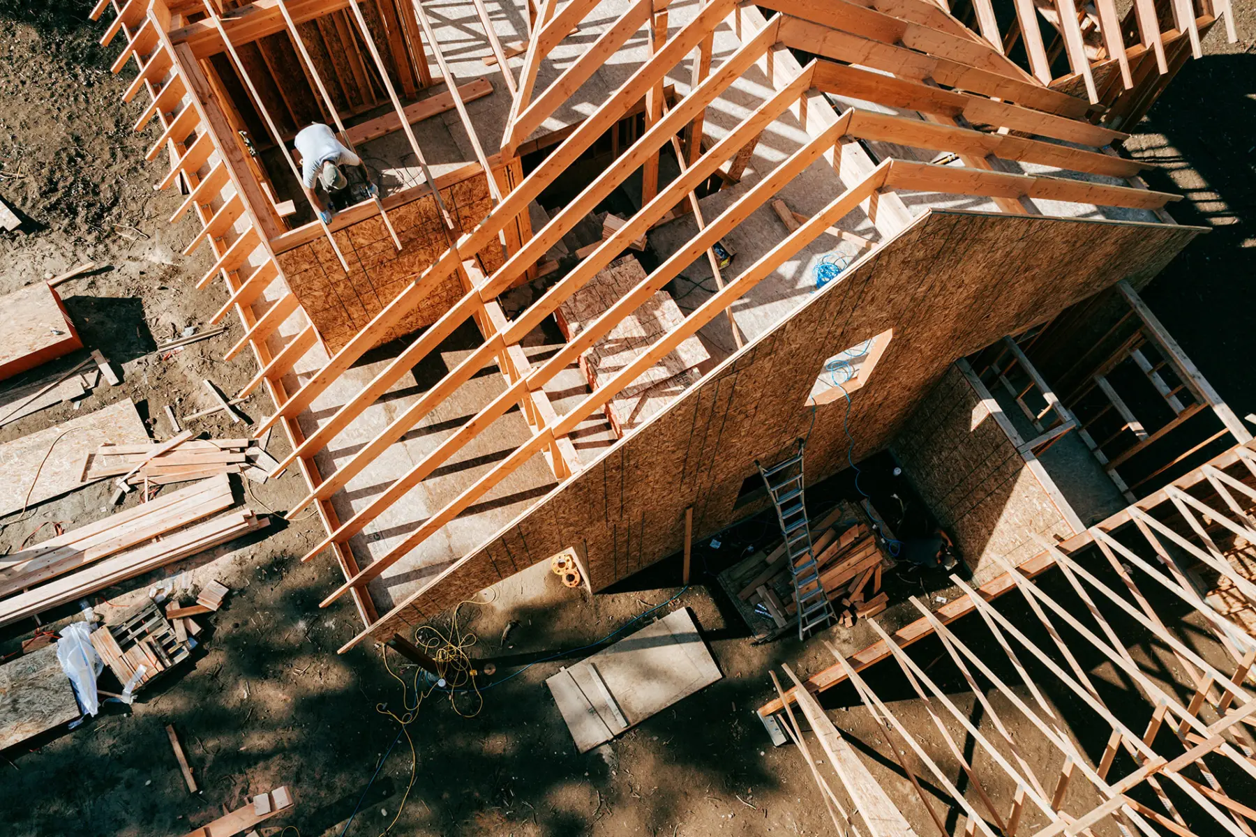 Construction site viewed from above, showcasing wooden framing and workers assembling a structure amid scattered materials and tools.