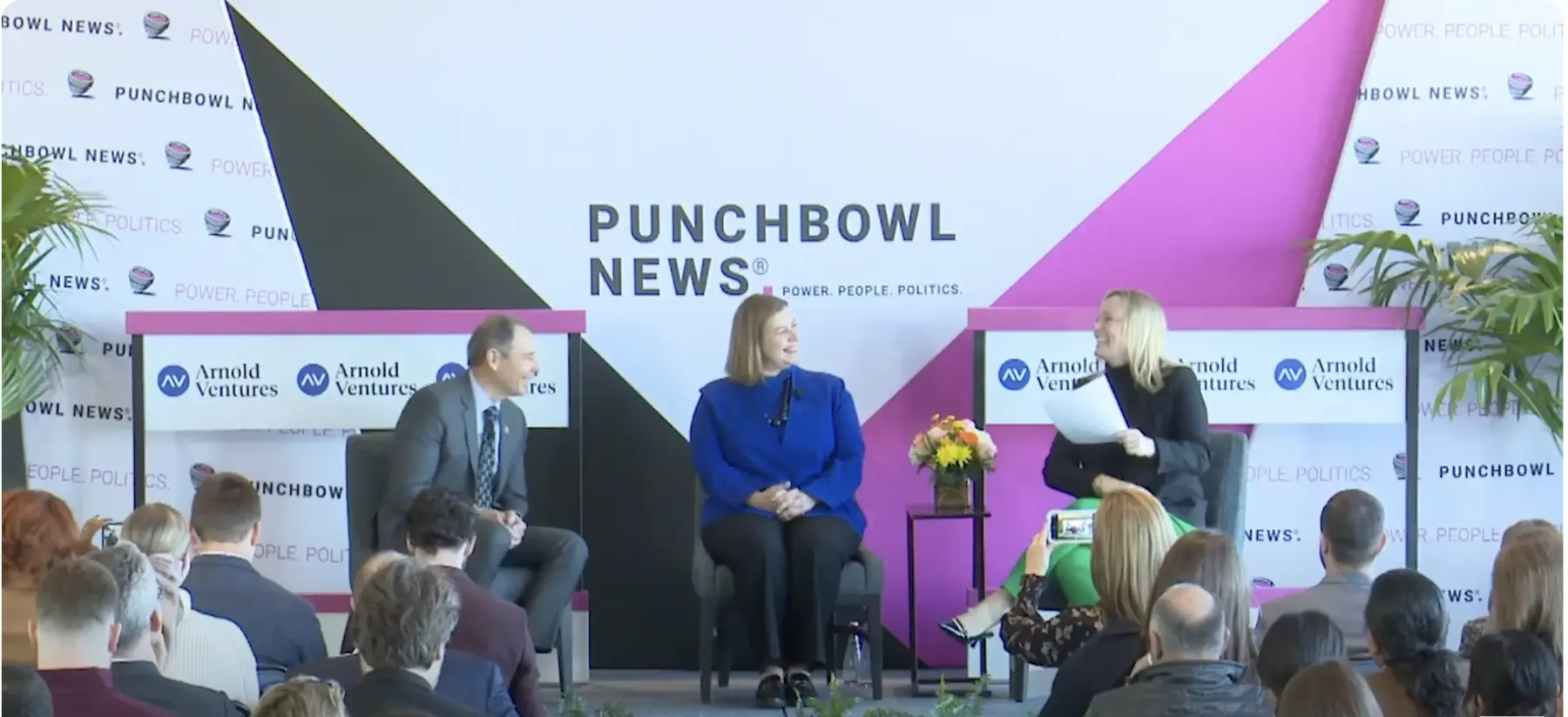 A lively panel discussion at Punchbowl News features three presenters seated on stage, engaging an attentive audience in a modern setting.