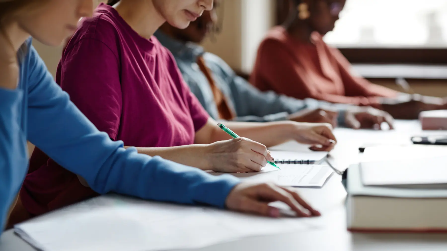 Four individuals are engaged in a study session, focused on writing notes in notebooks and textbooks on a table.