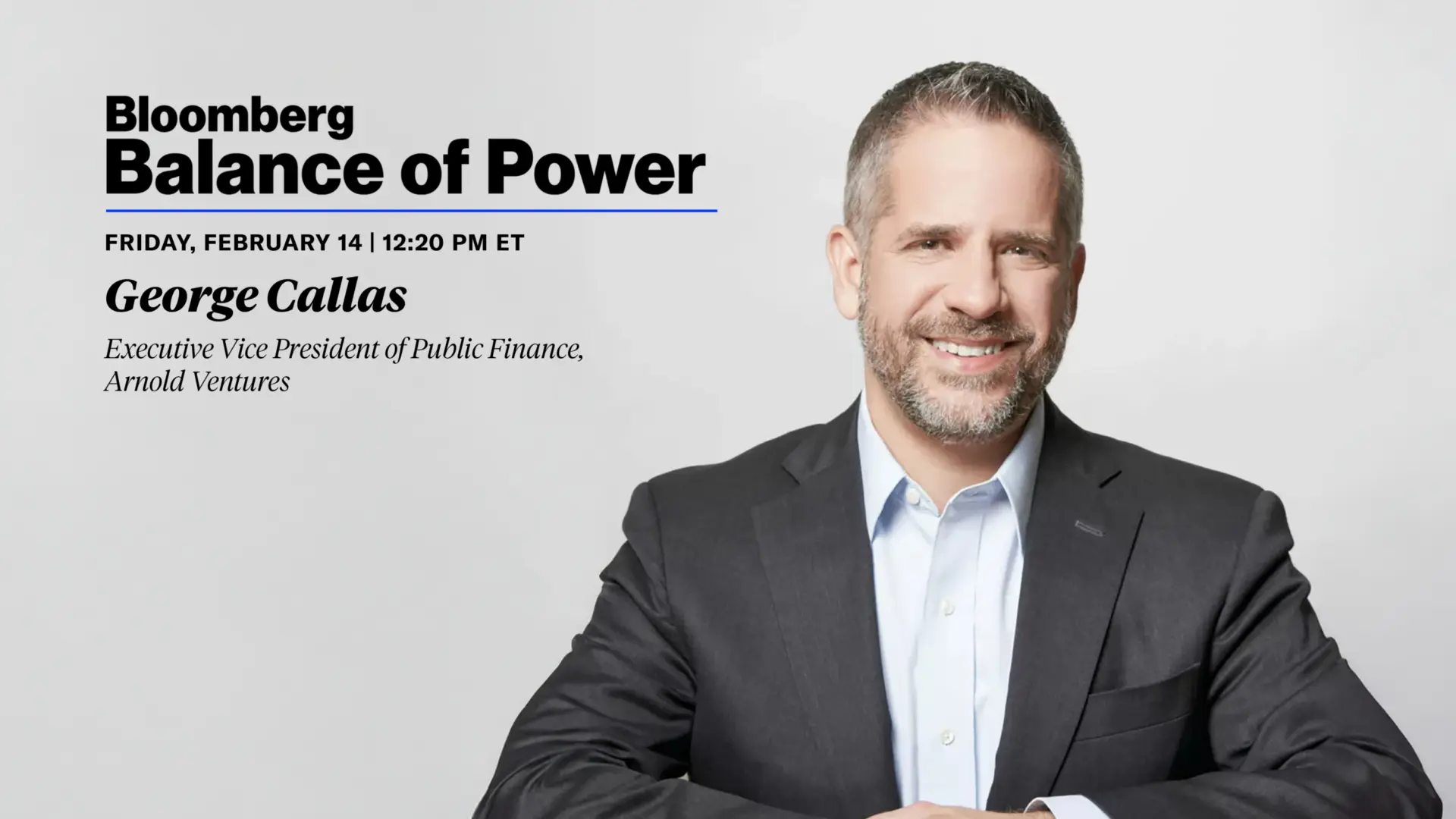 A smiling man in a dark suit and light shirt sits with arms crossed, presenting on Bloomberg's Balance of Power, February 14.
