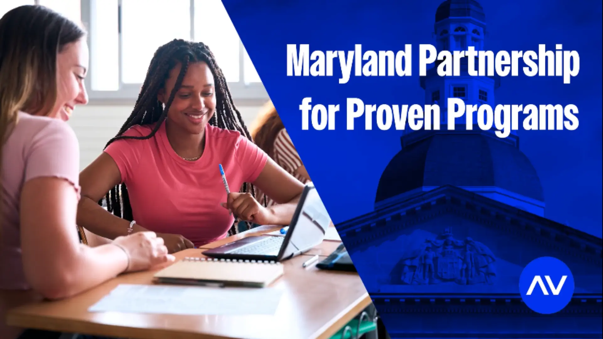 Two young women engage in a collaborative study session at a table, with a laptop open and Maryland's state building subtly in the background.
