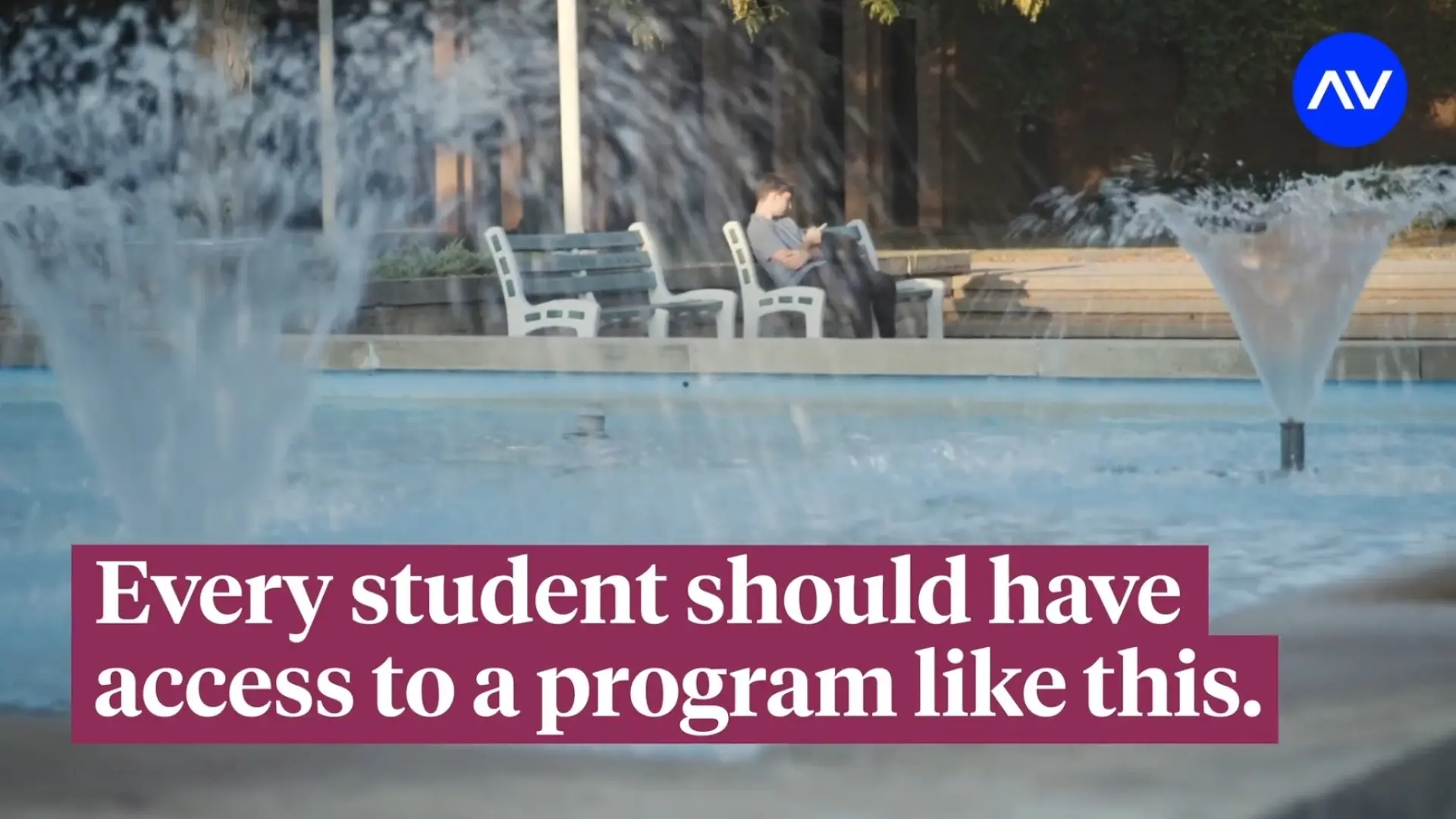 Fountain jets in a plaza with a person on a bench in the background and an overlaid caption about every student having access to a program.