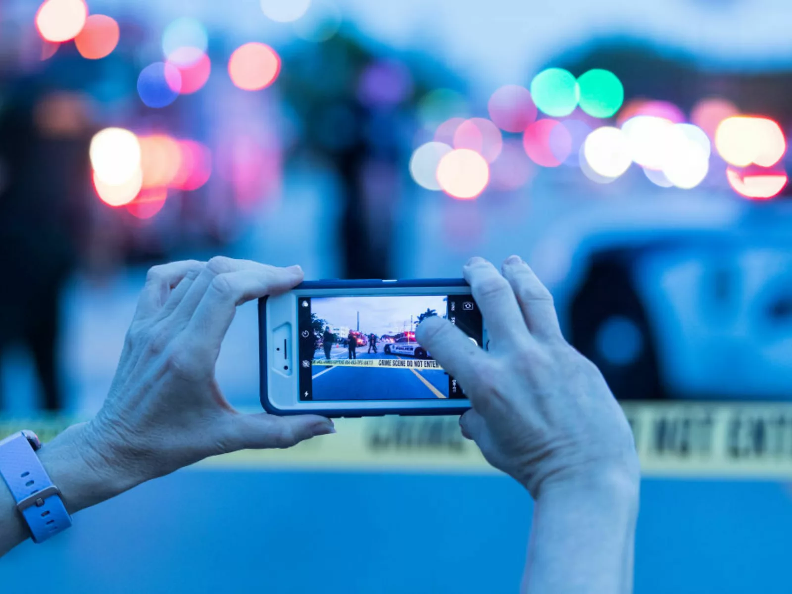 A journalist holds up a smartphone to take a photo of police tape and cards.