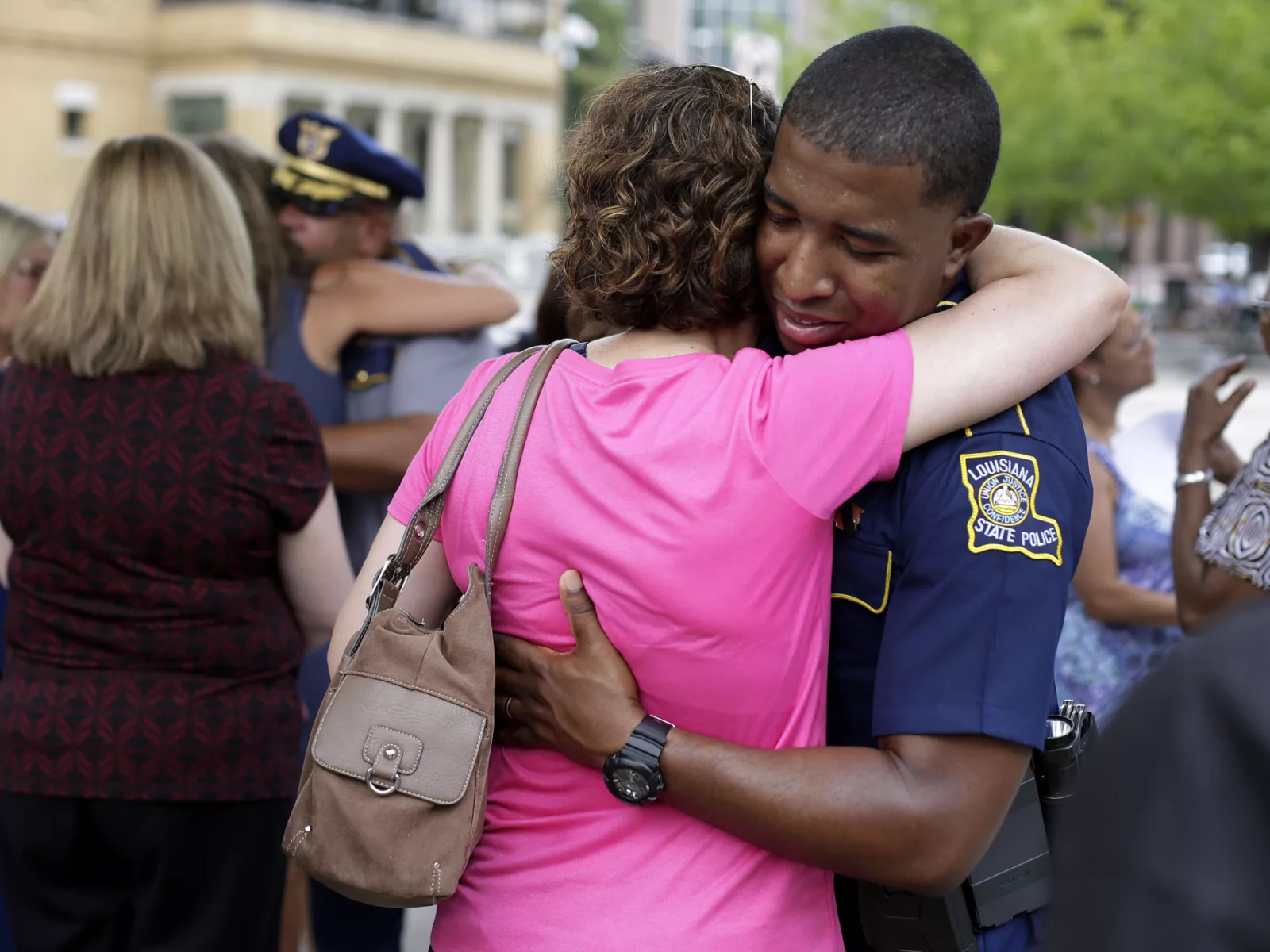 Black police officer from Baton Rouge hugs a white woman in a pink shirt.