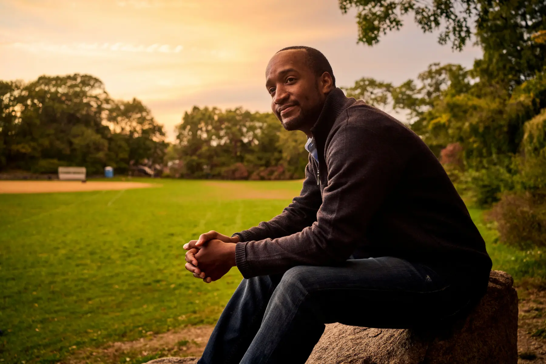 Rich Pierre sitting in a field with sunset in the background.
