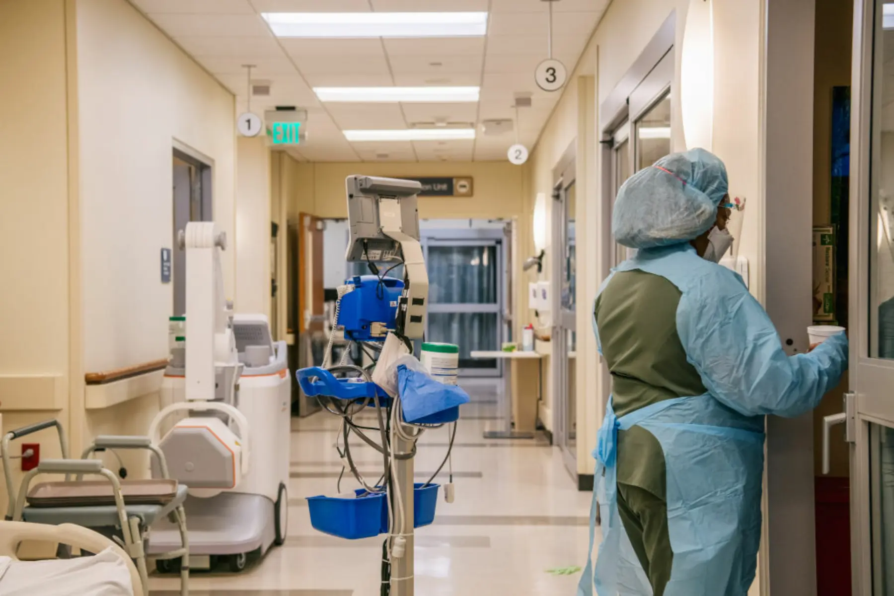 View of hospital corridor with machines and hospital worker in scrubs.