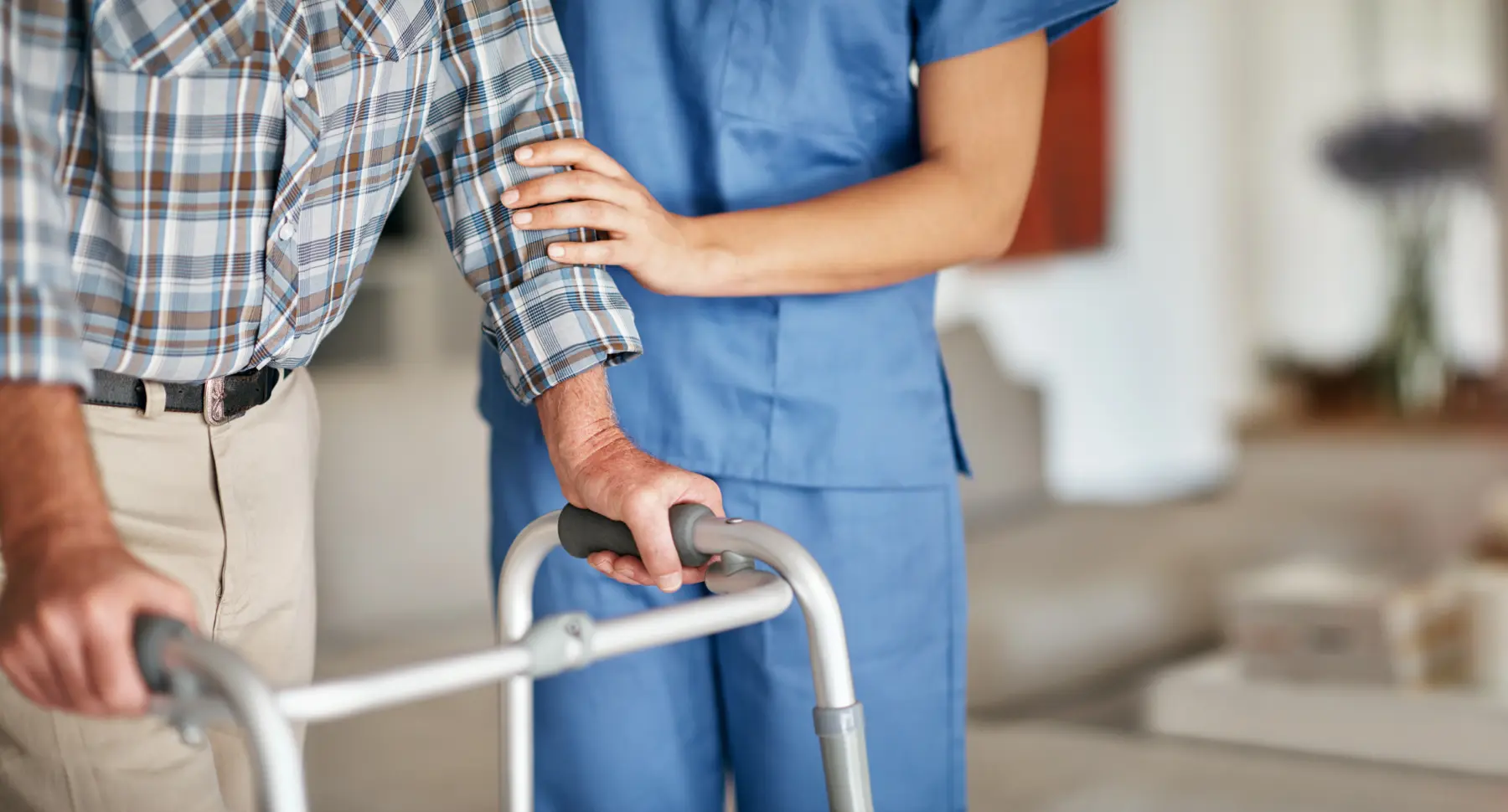 Nurse in scrubs helps guide patient using a walking aid