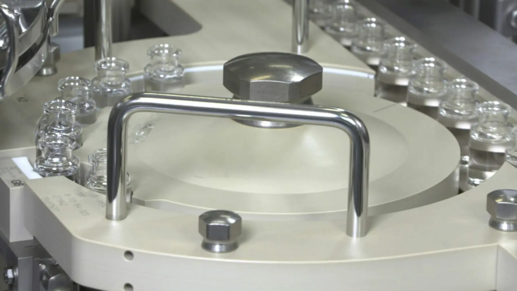 A close-up view of a circular industrial machine component with metallic and beige elements, surrounded by glass vials, showcasing precision engineering.