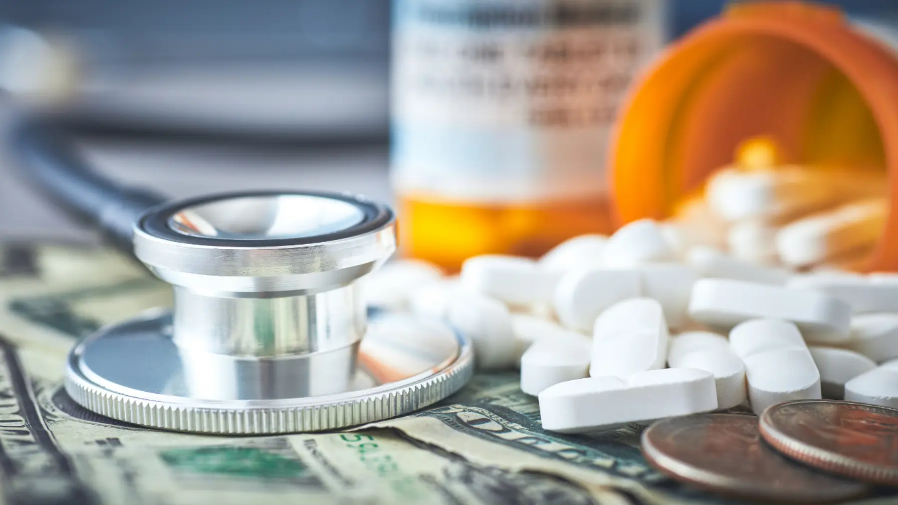 A stethoscope rests on dollar bills, surrounded by spilled white pills and a prescription bottle, highlighting healthcare costs.