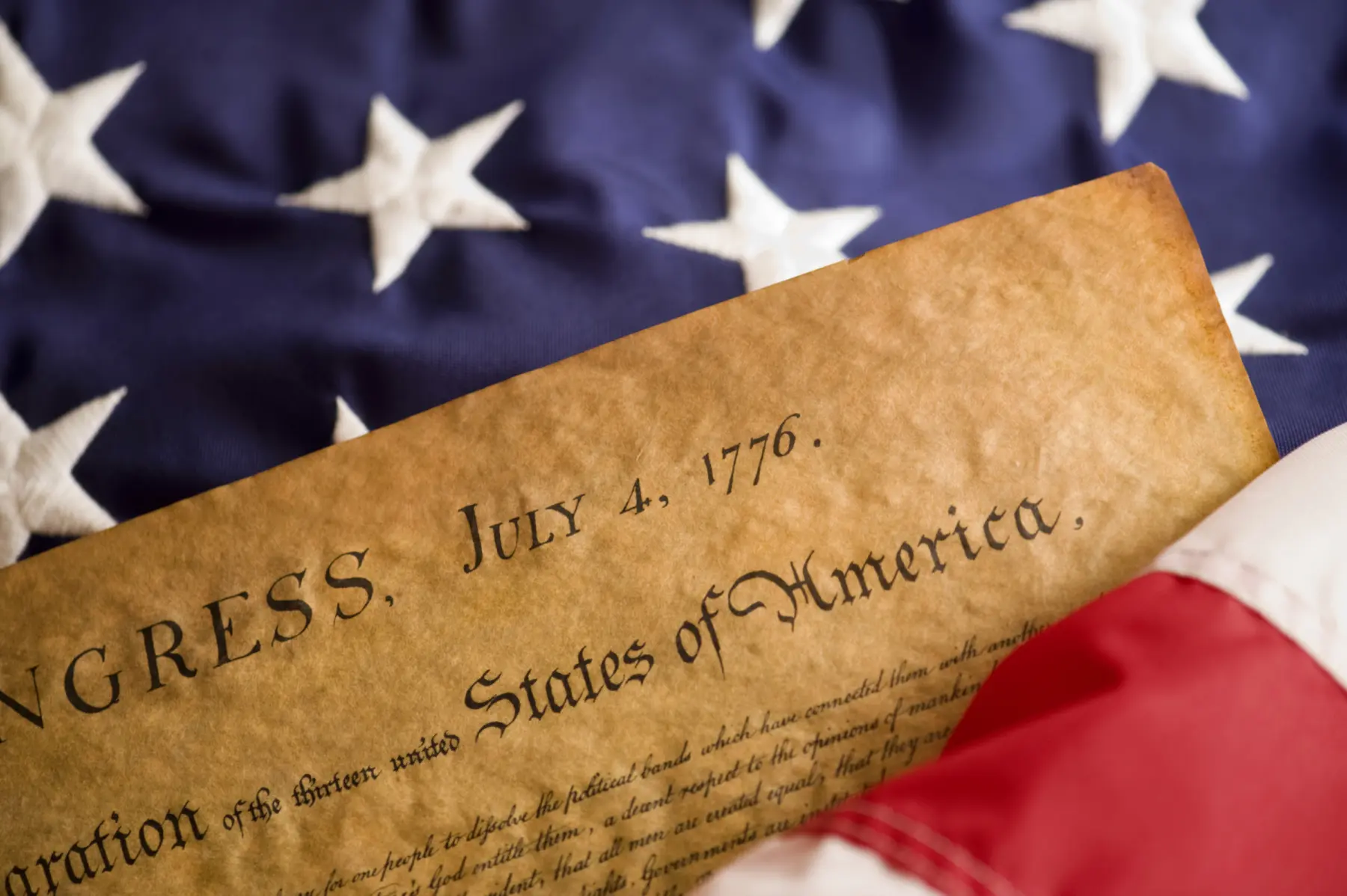 The Declaration of Independence partially rests on a folded American flag, showcasing its historic significance and patriotic colors.