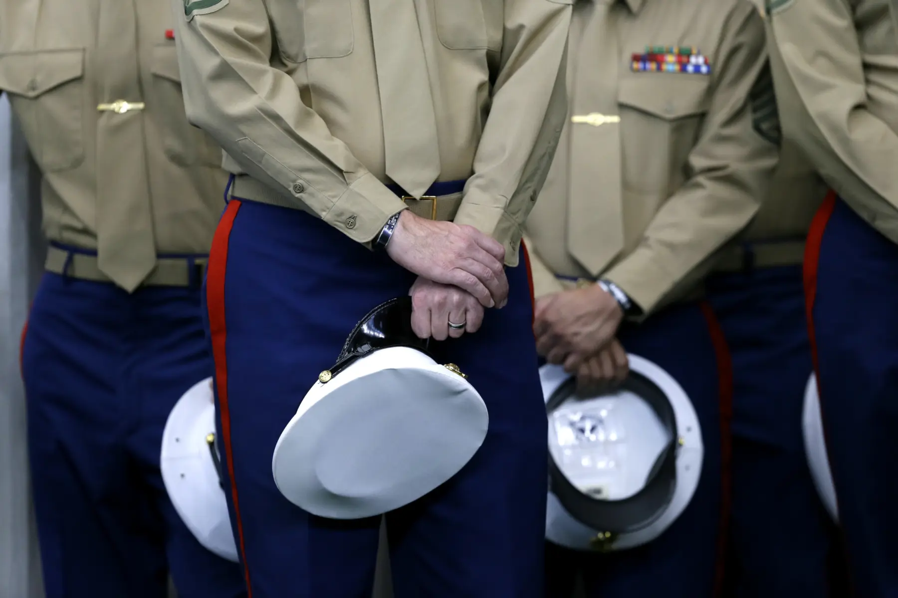 Members of a military unit stand in uniform, holding white hats with gold buttons, hands clasped, reflecting discipline and readiness.
