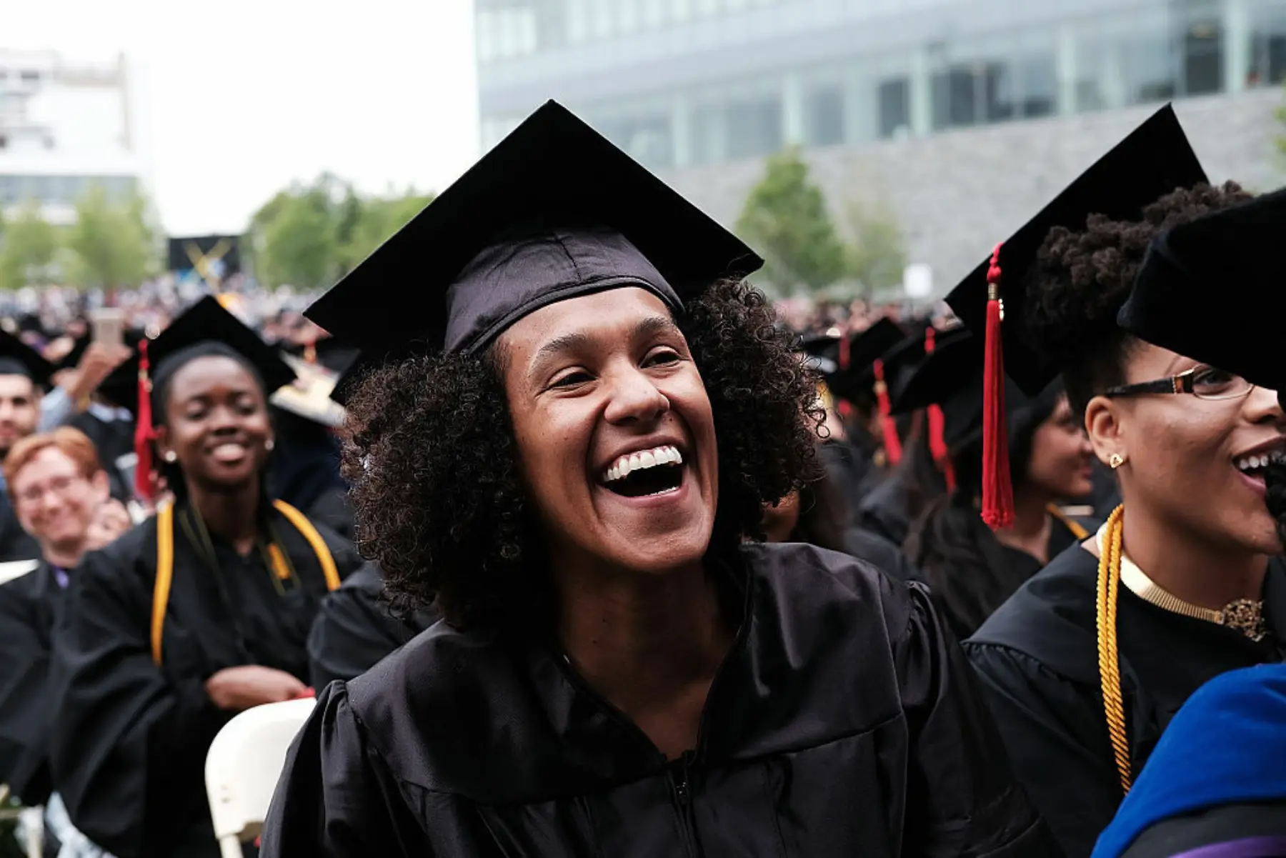 A graduate wearing a cap and gown smiles in a sea of classmates.