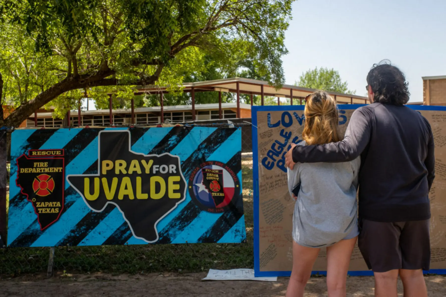 A couple stands in front of a sign that reads Pray for Uvalde.