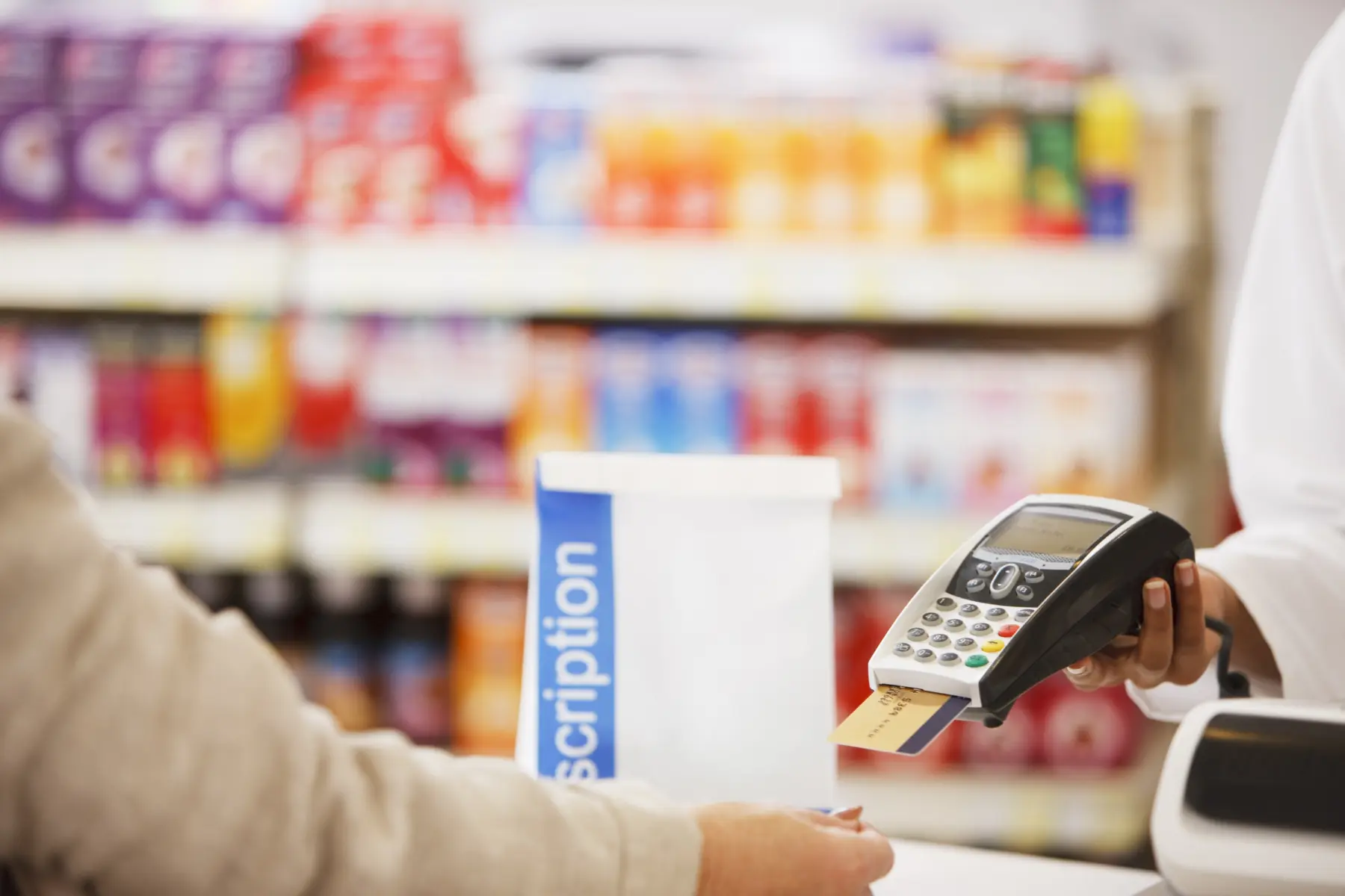 A customer approaches a register, ready to pay with a card at a pharmacy, surrounded by colorful product displays in the background.