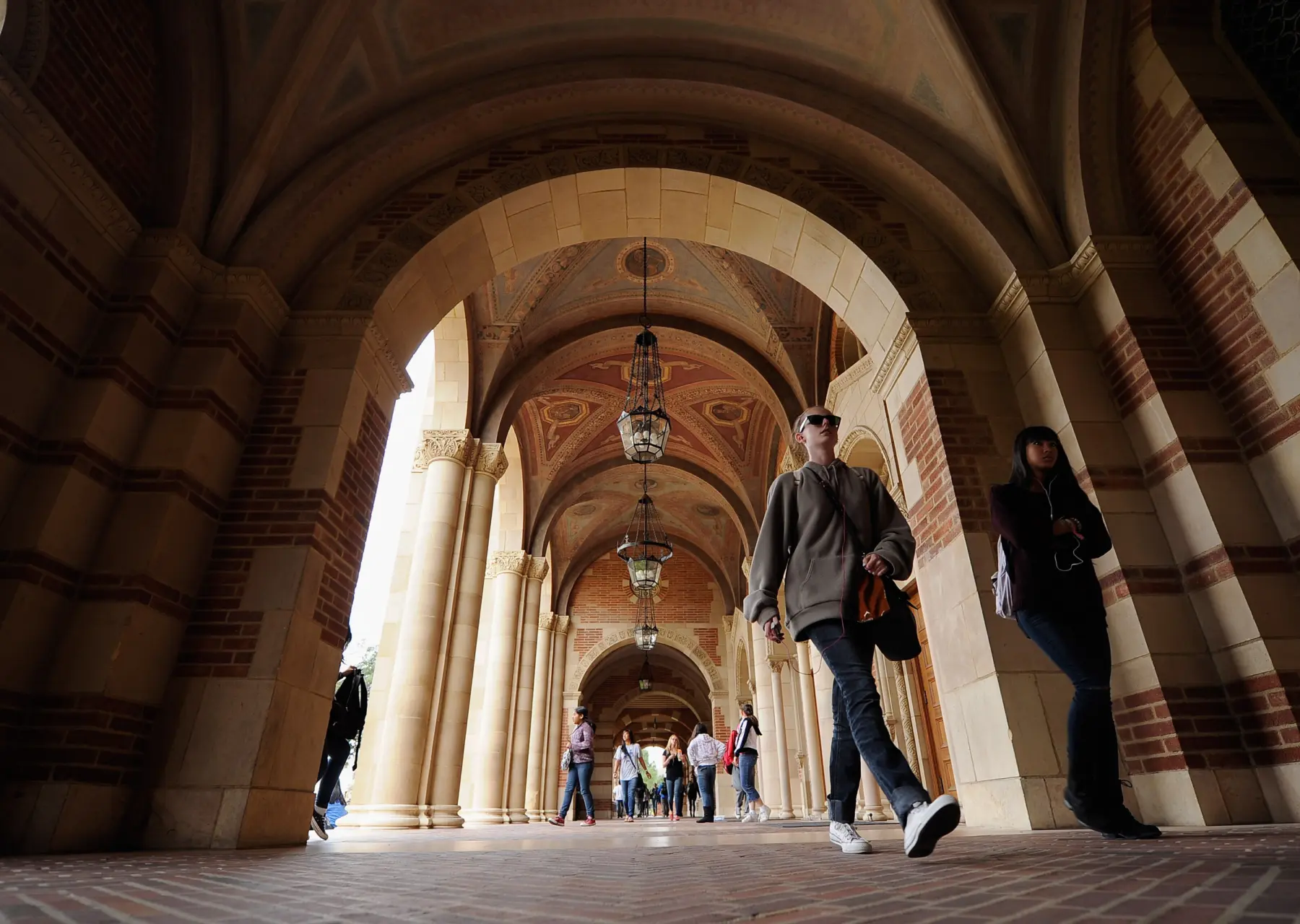 Under arched brick corridors, students walk beneath ornate ceilings and hanging lanterns, creating a vibrant campus atmosphere.