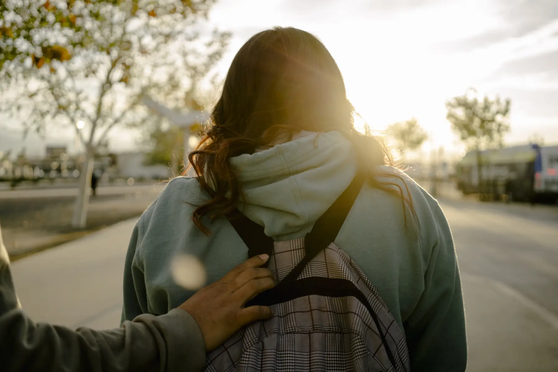 Melissa’s hand reaches out and holds onto Angie’s backpack as Angie walks toward the shining sun.