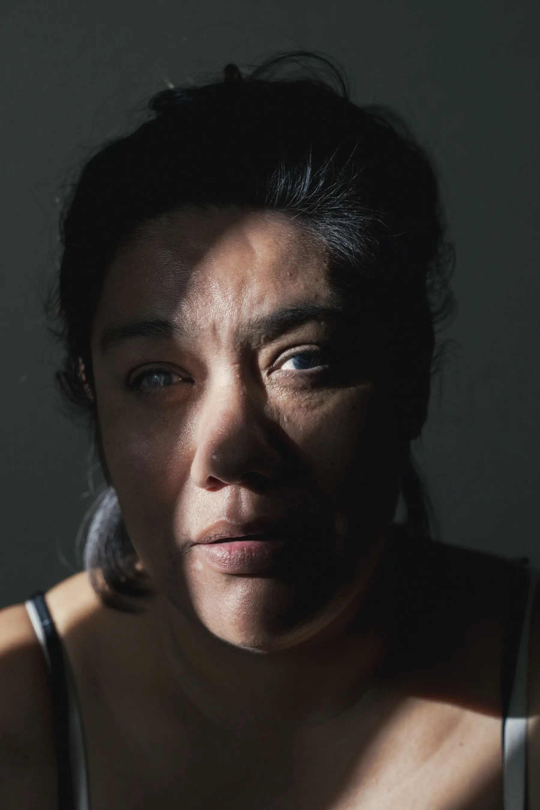 Melissa is seen close up looking toward the camera with a strip of light illuminating the right side of her face.