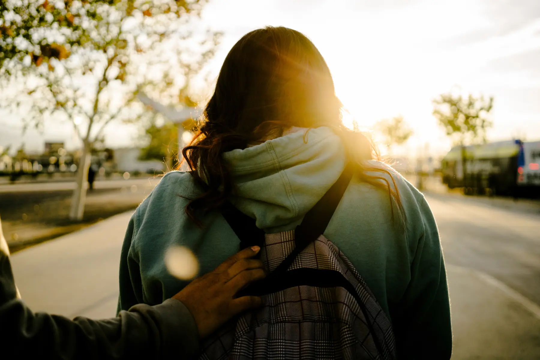 Melissa’s hand reaches out and holds onto Angie’s backpack as Angie walks toward the shining sun.