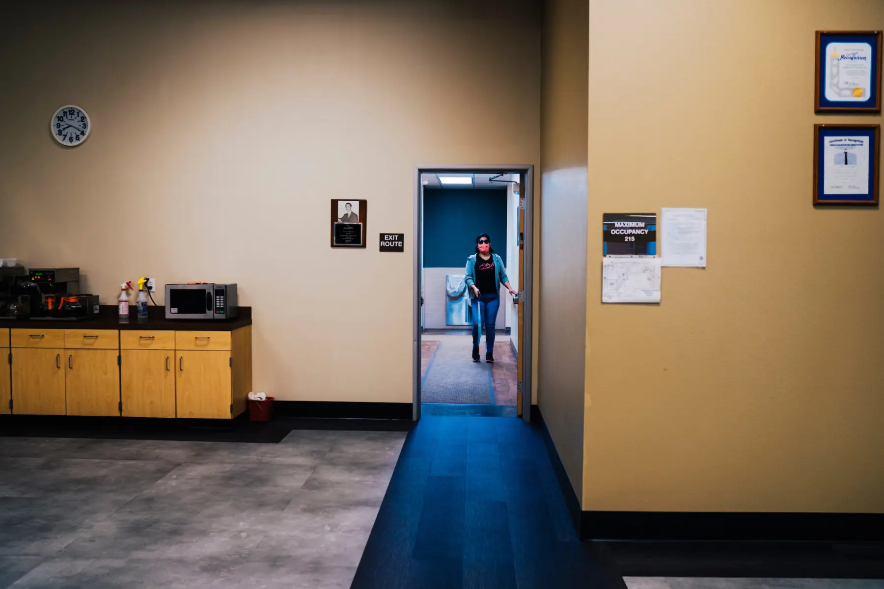 Melissa is seen in the distance as she holds onto a wall while making her way toward a doorway inside an office-like building.