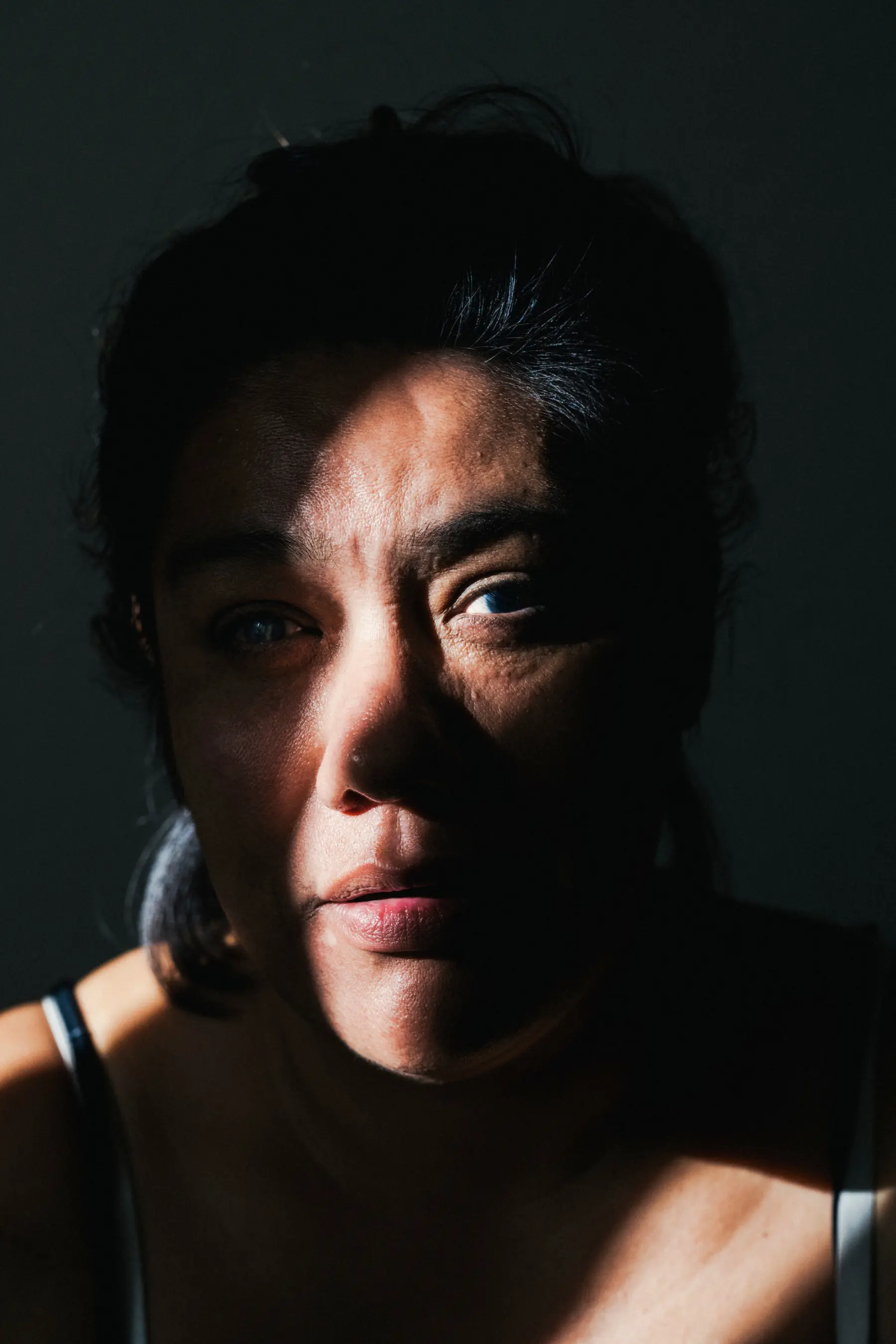 Melissa is seen close up looking toward the camera with a strip of light illuminating the right side of her face.