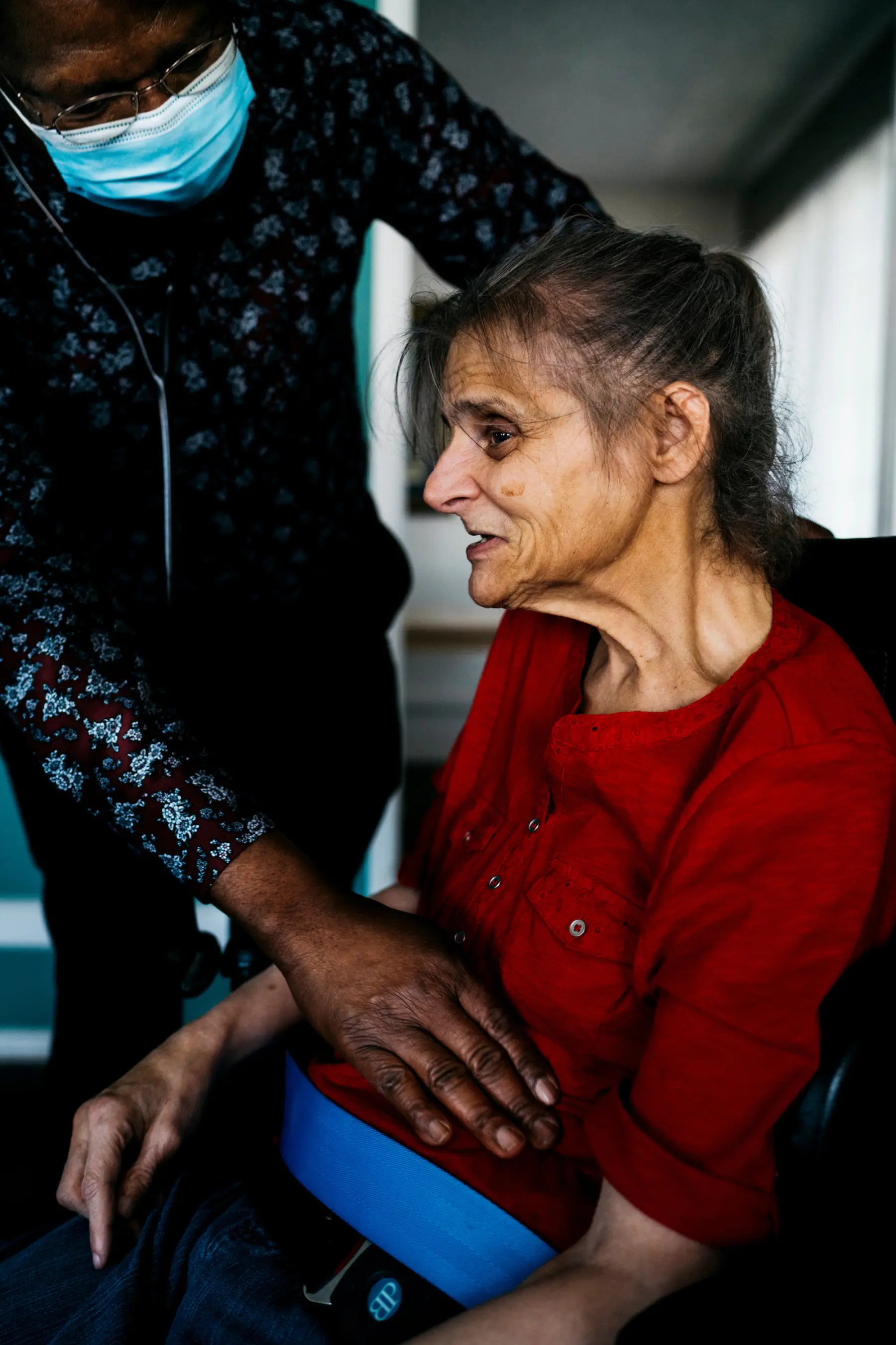 Nurse practitioner Dennis, an older Black male, leans over Ann and presses on her stomach with one hand. The nurse practitioner wears a surgical mask and has a stethoscope around his neck.